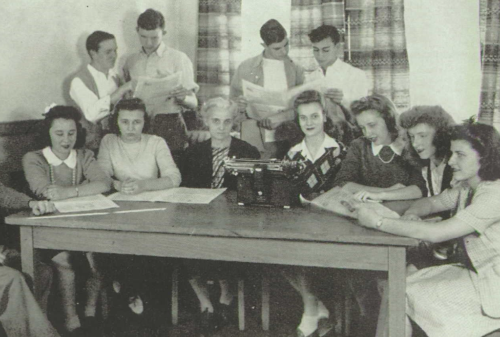 Dorothy Stoutzenberg, Faculty Sponsor to the school newspaper (center, behind the typewriter).